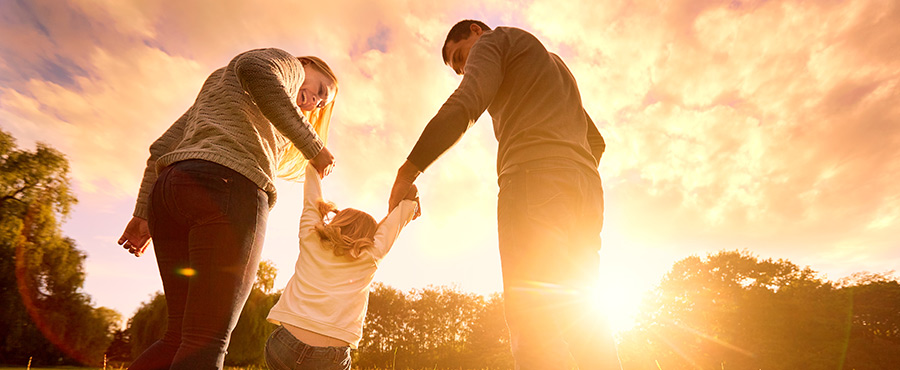 familia feliz paseando al atardecer en un parque. El concepto de familia feliz. Los padres se toman las manos del bebé.